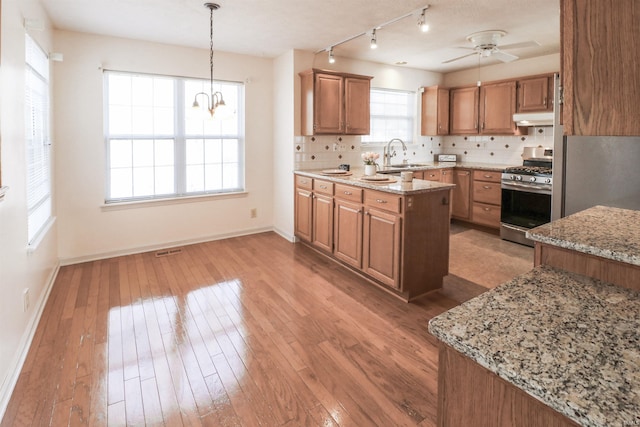 kitchen with under cabinet range hood, light wood-style flooring, stainless steel gas range, and tasteful backsplash