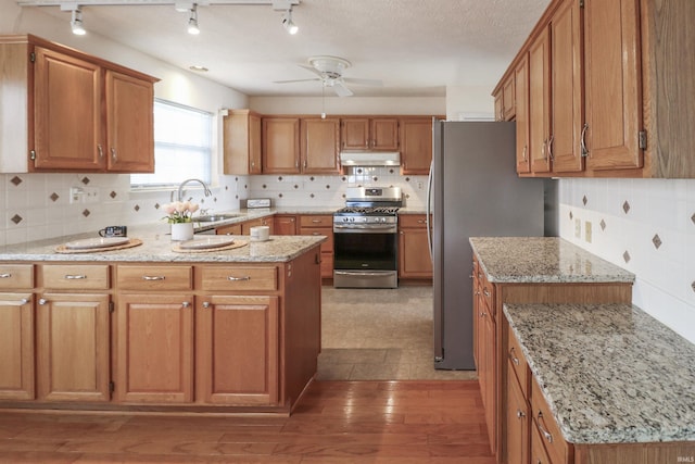 kitchen featuring a peninsula, ceiling fan, a sink, under cabinet range hood, and appliances with stainless steel finishes