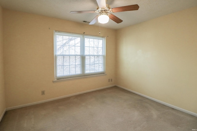 carpeted spare room with visible vents, baseboards, and a ceiling fan