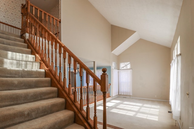 stairway with visible vents, baseboards, and high vaulted ceiling