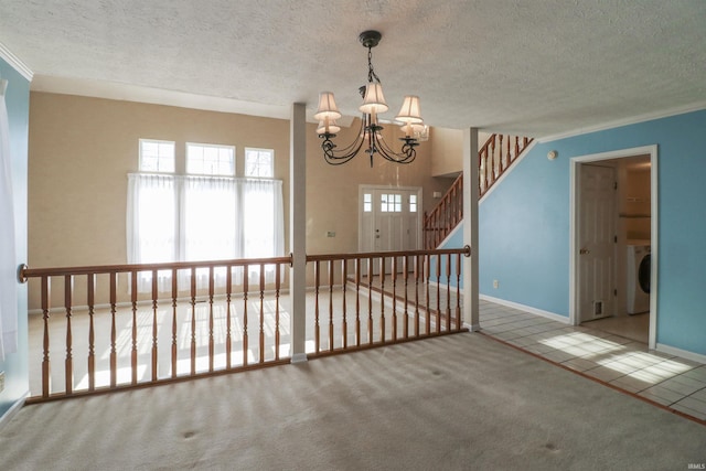 tiled empty room with carpet, washer / clothes dryer, a textured ceiling, crown molding, and a notable chandelier