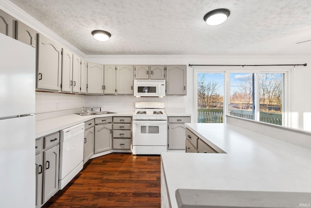 kitchen featuring dark wood-style flooring, backsplash, white appliances, and a sink