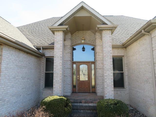 doorway to property with brick siding and roof with shingles