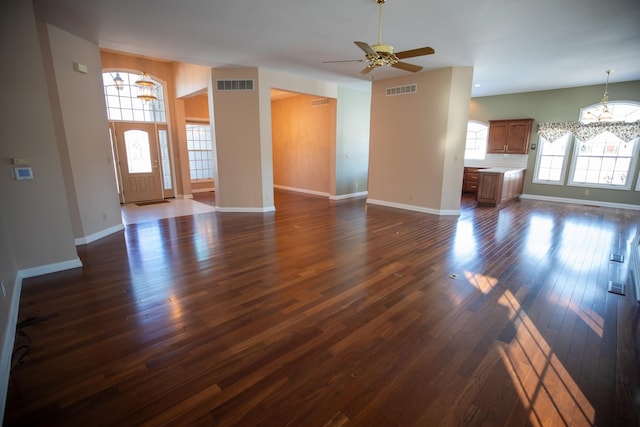 unfurnished living room with visible vents, ceiling fan with notable chandelier, dark wood-type flooring, and baseboards