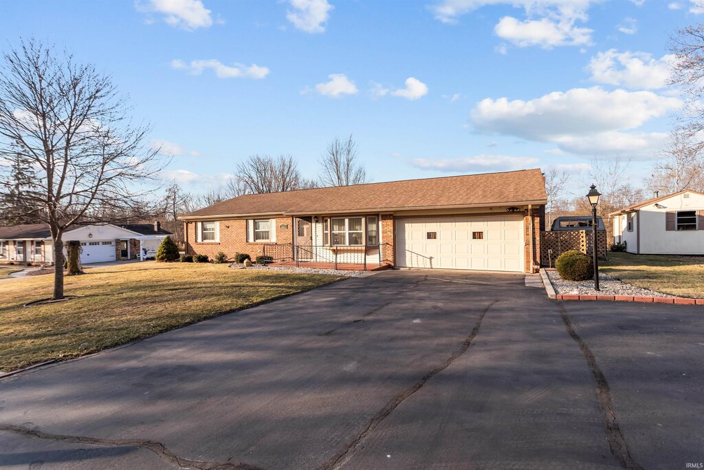 ranch-style home featuring a front lawn, aphalt driveway, roof with shingles, an attached garage, and brick siding