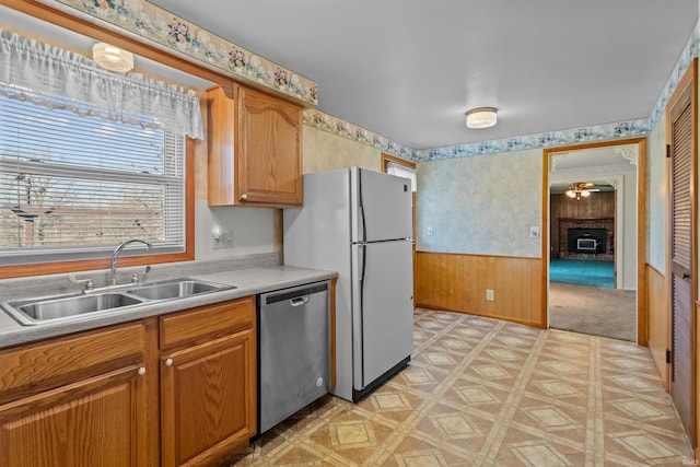 kitchen featuring wallpapered walls, a wainscoted wall, light floors, stainless steel dishwasher, and a sink