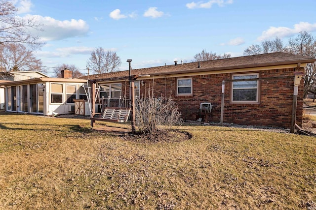 rear view of property featuring a yard, brick siding, a chimney, and a sunroom