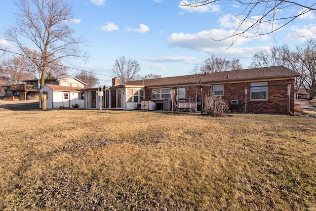 rear view of property featuring a yard, brick siding, a chimney, and a sunroom