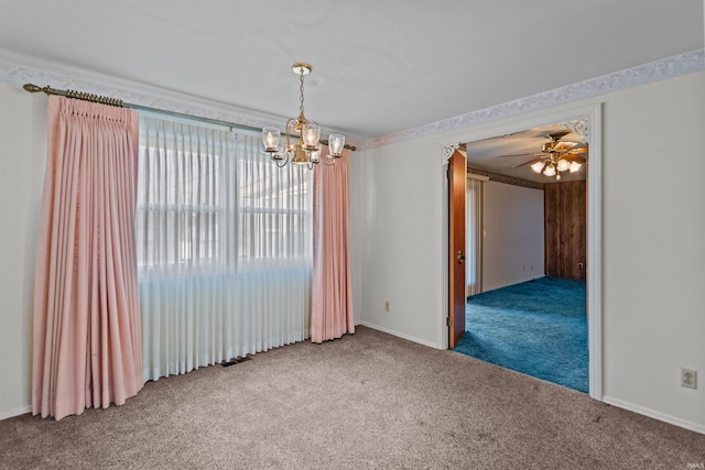 carpeted spare room featuring ceiling fan with notable chandelier and baseboards