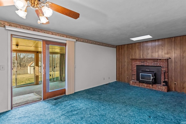 unfurnished living room featuring carpet flooring, wood walls, and a wood stove