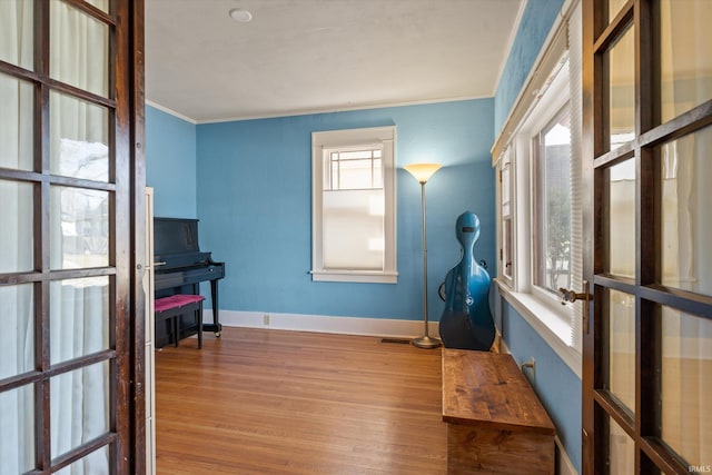 interior space featuring baseboards, wood finished floors, visible vents, and ornamental molding