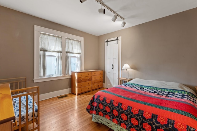 bedroom with visible vents, wood finished floors, a barn door, rail lighting, and baseboards