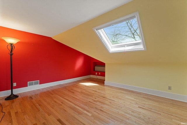 additional living space with visible vents, baseboards, a wall mounted air conditioner, vaulted ceiling with skylight, and wood finished floors