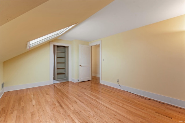 bonus room featuring vaulted ceiling with skylight, built in features, baseboards, and light wood-type flooring