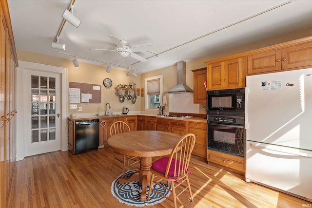 kitchen featuring black appliances, light wood-style flooring, a sink, wall chimney exhaust hood, and ceiling fan