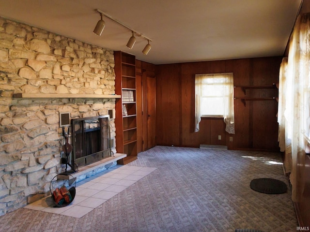 unfurnished living room with a stone fireplace, wood walls, and carpet flooring