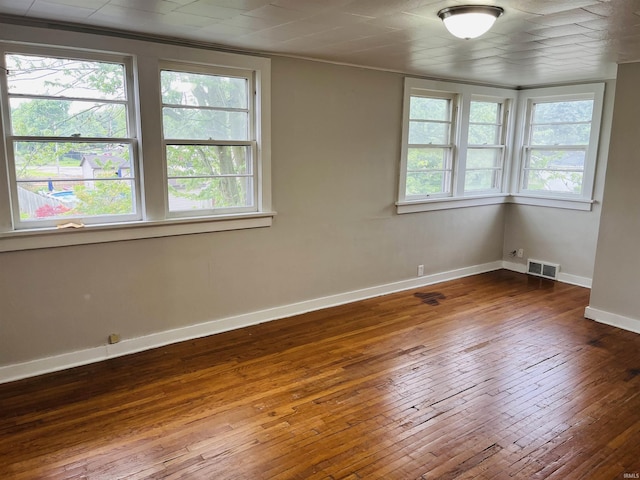 empty room featuring visible vents, plenty of natural light, baseboards, and hardwood / wood-style floors