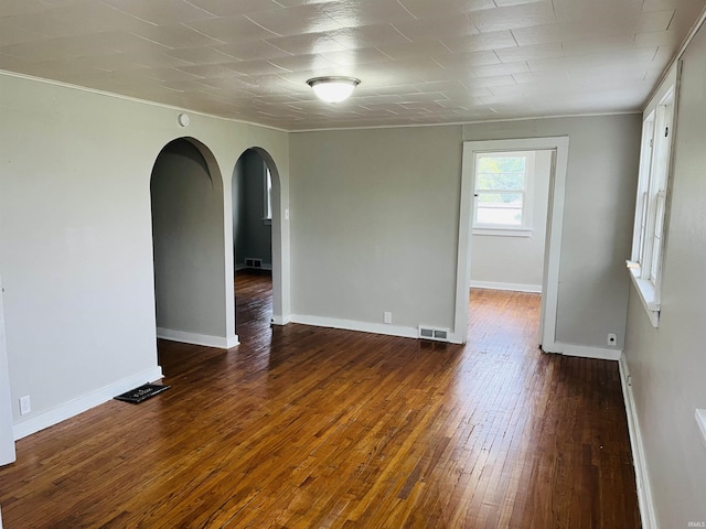 unfurnished room featuring visible vents, arched walkways, baseboards, and hardwood / wood-style flooring