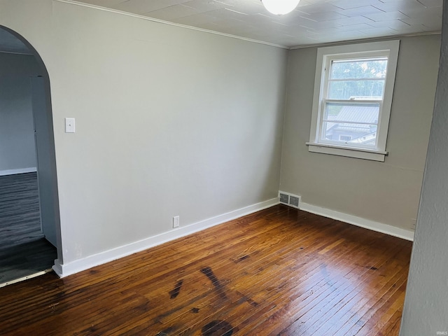 spare room featuring visible vents, dark wood-type flooring, baseboards, ornamental molding, and arched walkways