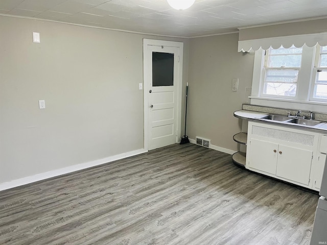 kitchen featuring visible vents, light wood-type flooring, ornamental molding, white cabinetry, and a sink