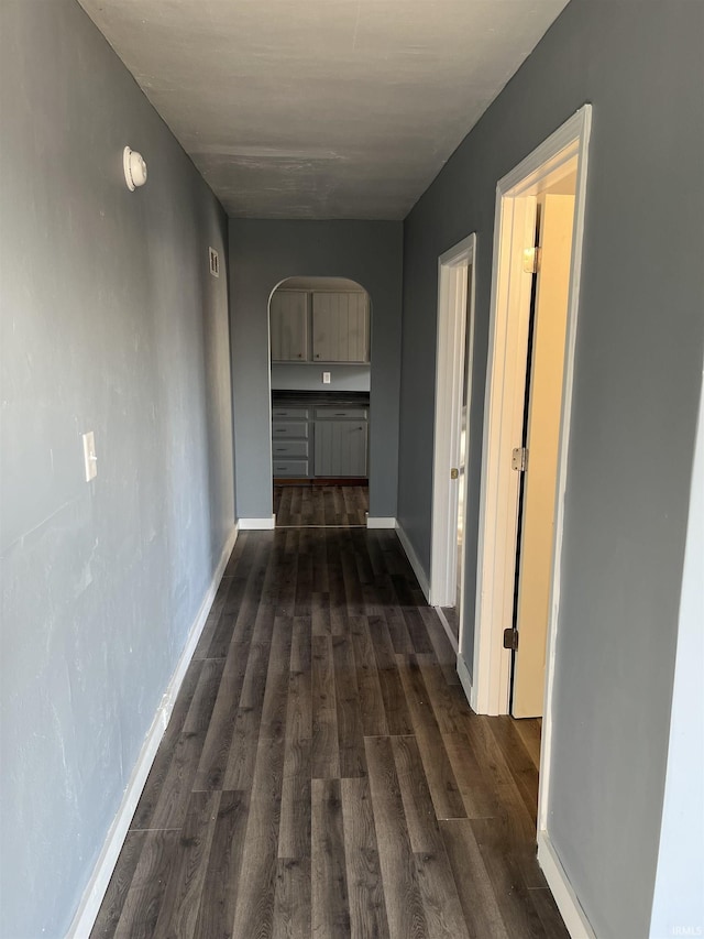 corridor with arched walkways, baseboards, and dark wood-style flooring