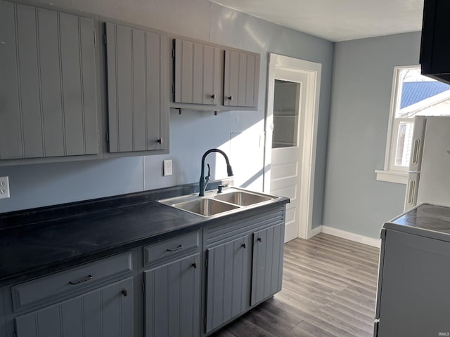 kitchen with freestanding refrigerator, gray cabinetry, a sink, dark countertops, and range