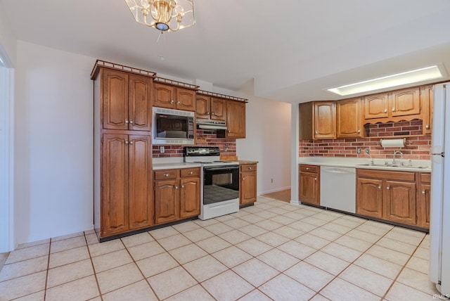 kitchen with under cabinet range hood, light countertops, brown cabinetry, white appliances, and a sink