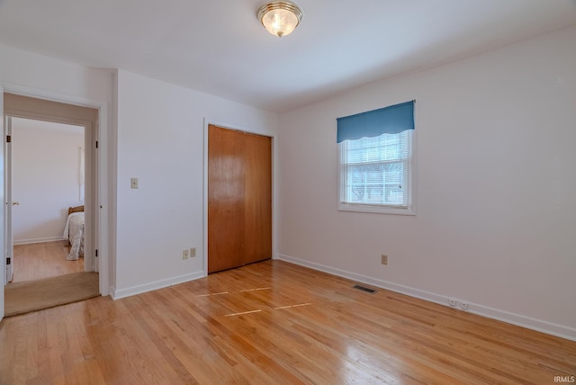 unfurnished bedroom with a closet, visible vents, light wood-style flooring, and baseboards