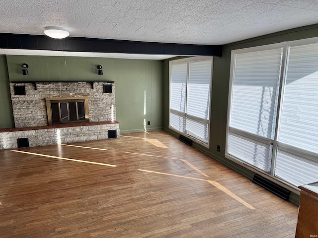 unfurnished living room featuring visible vents, a textured ceiling, baseboards, and wood finished floors