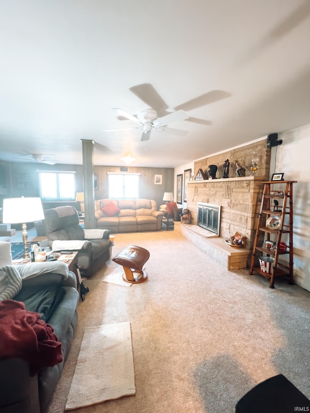 carpeted living area featuring a stone fireplace and ceiling fan