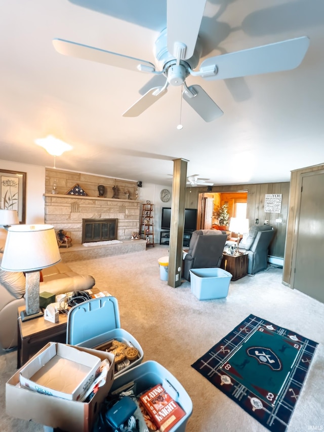 carpeted living area with wooden walls, baseboard heating, ceiling fan, and a fireplace