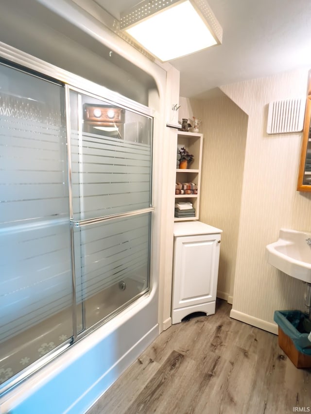 bathroom featuring wood finished floors and shower / bath combination with glass door