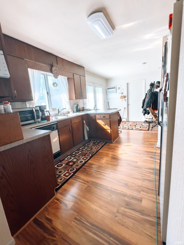 kitchen with dishwashing machine, light wood finished floors, a peninsula, a sink, and stainless steel microwave