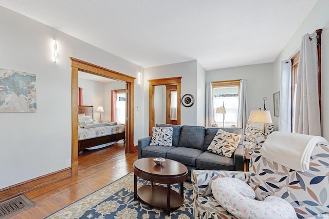 living room featuring visible vents, a textured ceiling, light wood-type flooring, and baseboards