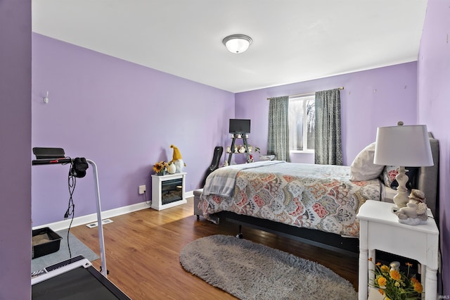 bedroom featuring a glass covered fireplace, visible vents, baseboards, and wood finished floors