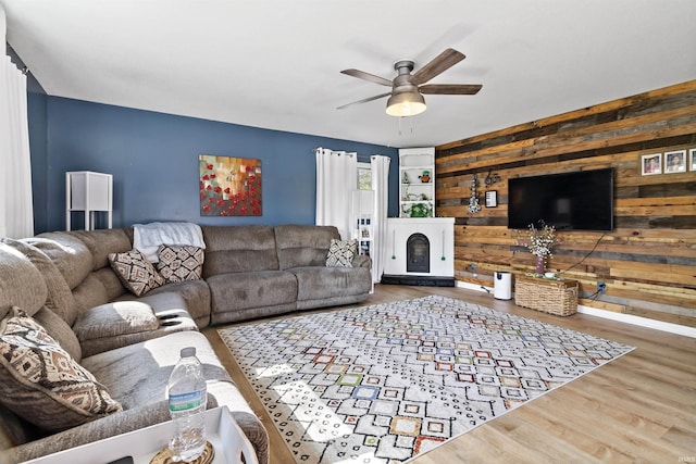 living area with wooden walls, a ceiling fan, and wood finished floors