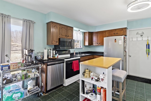 kitchen with dark tile patterned flooring, a sink, open shelves, appliances with stainless steel finishes, and a breakfast bar area