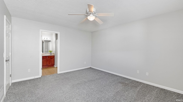 unfurnished bedroom featuring ensuite bath, light colored carpet, a textured ceiling, and baseboards