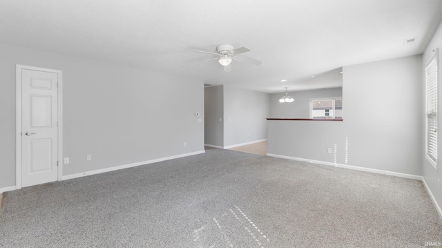 carpeted spare room featuring ceiling fan with notable chandelier, visible vents, and baseboards