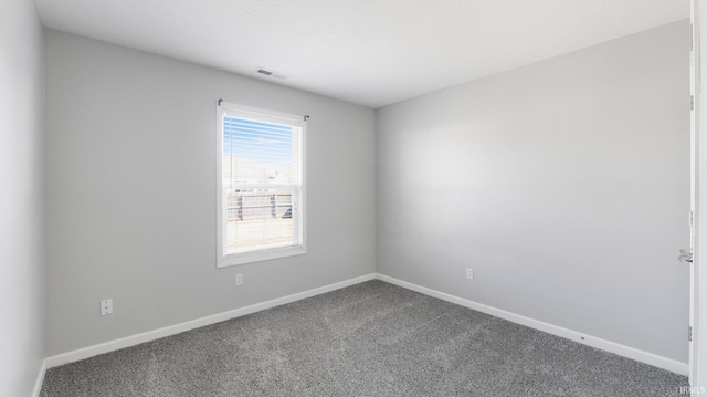 spare room featuring visible vents, baseboards, and dark colored carpet