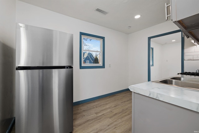 kitchen featuring baseboards, visible vents, light wood-style flooring, freestanding refrigerator, and light countertops