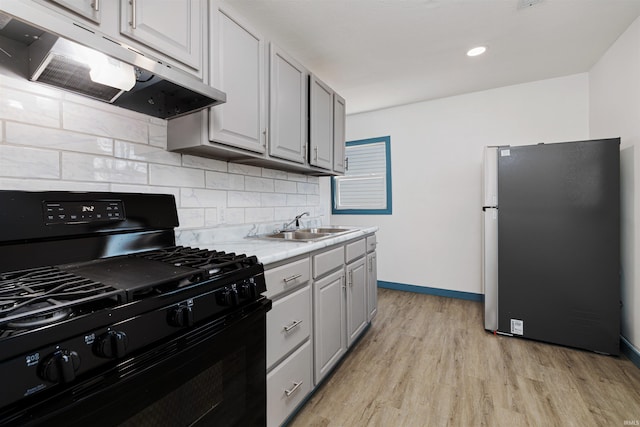 kitchen featuring under cabinet range hood, a sink, tasteful backsplash, freestanding refrigerator, and black range with gas stovetop