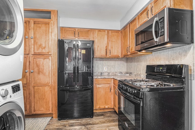 kitchen featuring decorative backsplash, black appliances, wood finished floors, and stacked washer and clothes dryer