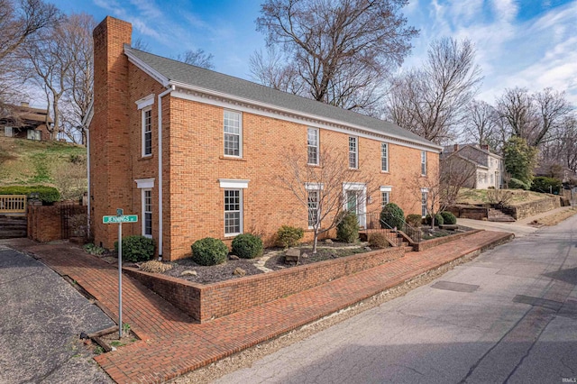 view of front of home with fence, brick siding, and a chimney