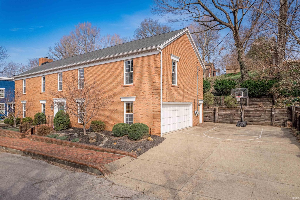 view of side of home featuring brick siding, an attached garage, fence, a chimney, and driveway