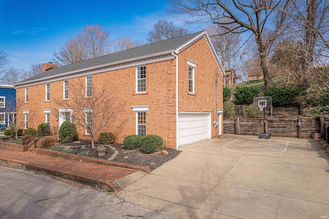 view of side of home featuring brick siding, an attached garage, fence, a chimney, and driveway