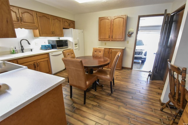 kitchen featuring a sink, dark wood-style floors, white appliances, brown cabinetry, and light countertops