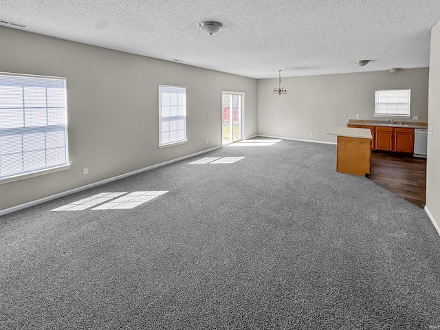 unfurnished living room with baseboards, visible vents, an inviting chandelier, a textured ceiling, and dark colored carpet