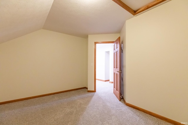 spare room featuring baseboards, light carpet, a textured ceiling, and vaulted ceiling