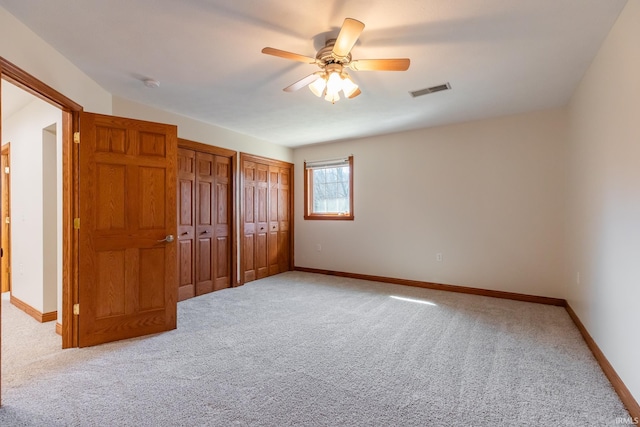 unfurnished bedroom with visible vents, light colored carpet, two closets, and baseboards